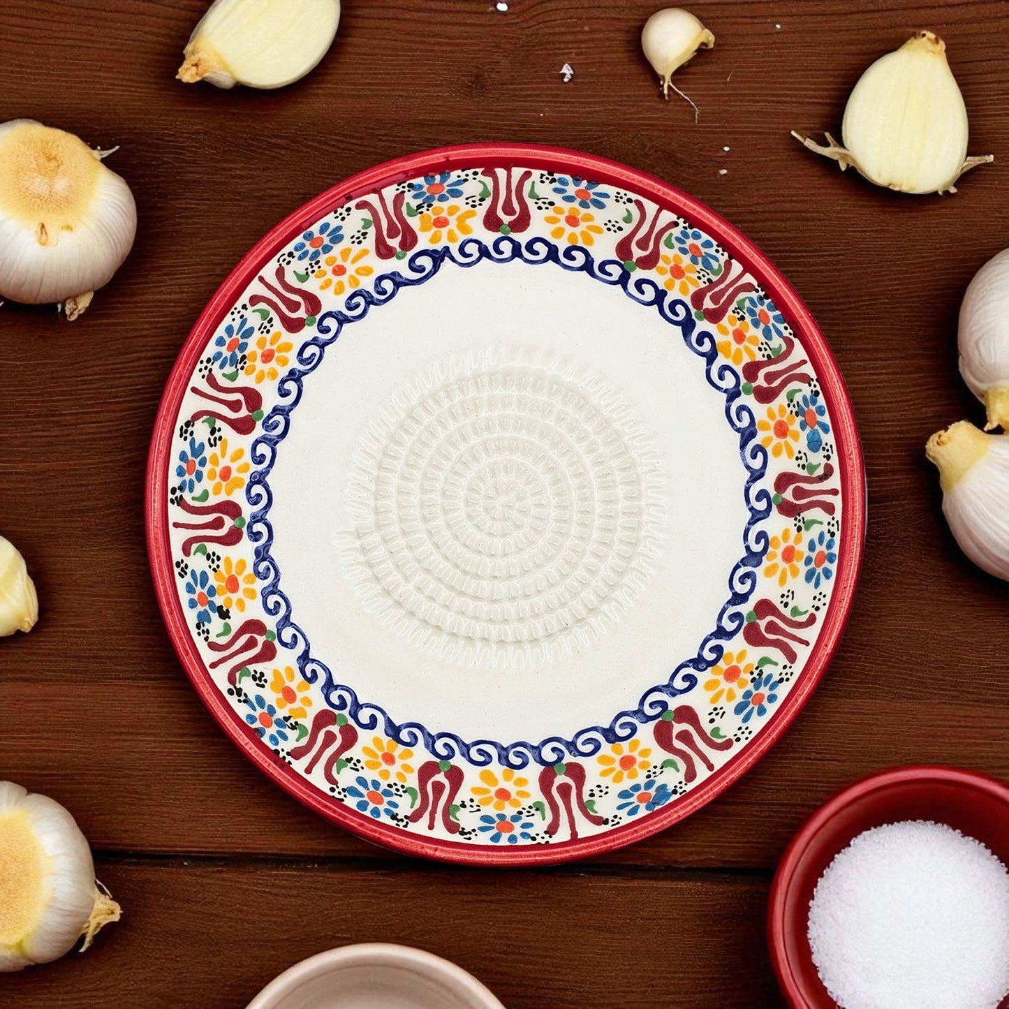 Decorative garlic grater bowl with colorful on a wooden surface with garlic bulbs.