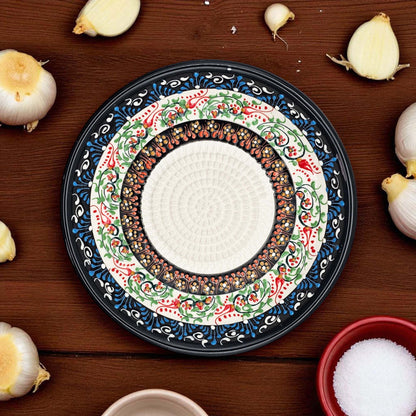 Decorative garlic grater bowl with intricate patterns on a wooden surface with garlic bulbs and a bowl of salt.