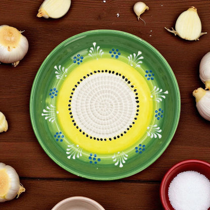 Decorative ceramic garlic grater bowl with green rim and yellow center on a wooden surface with garlic bulbs.