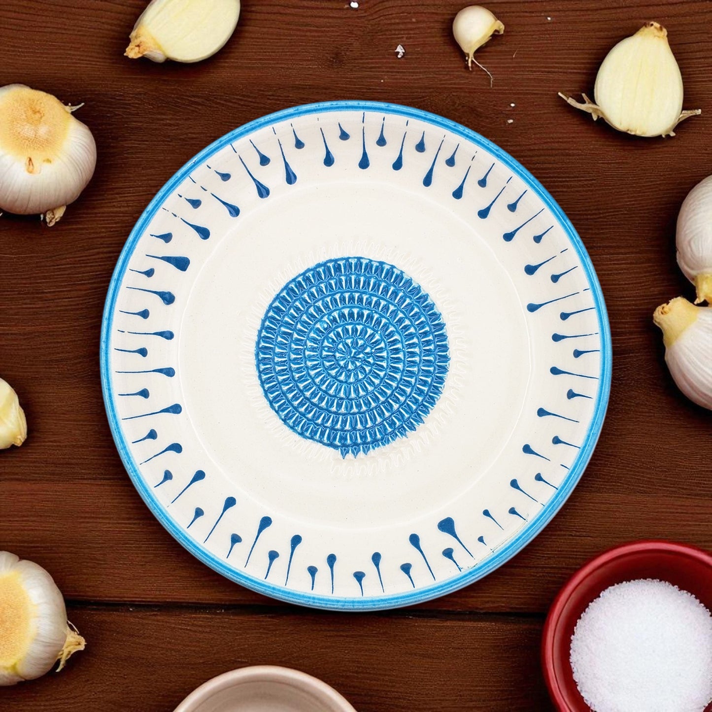 Decorative garlic grater bowl with blue and white pattern on a wooden surface with garlic bulbs.