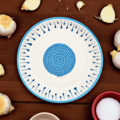 Decorative garlic grater bowl with blue and white pattern on a wooden surface with garlic bulbs.