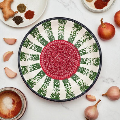 Decorative garlic grater bowl with a red center and green and white pattern on a marble surface with ingredients.