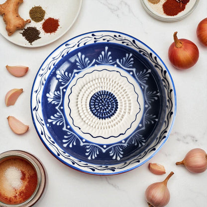 Decorative blue and white ceramic garlic grater bowl on a marble surface with ingredients around it.