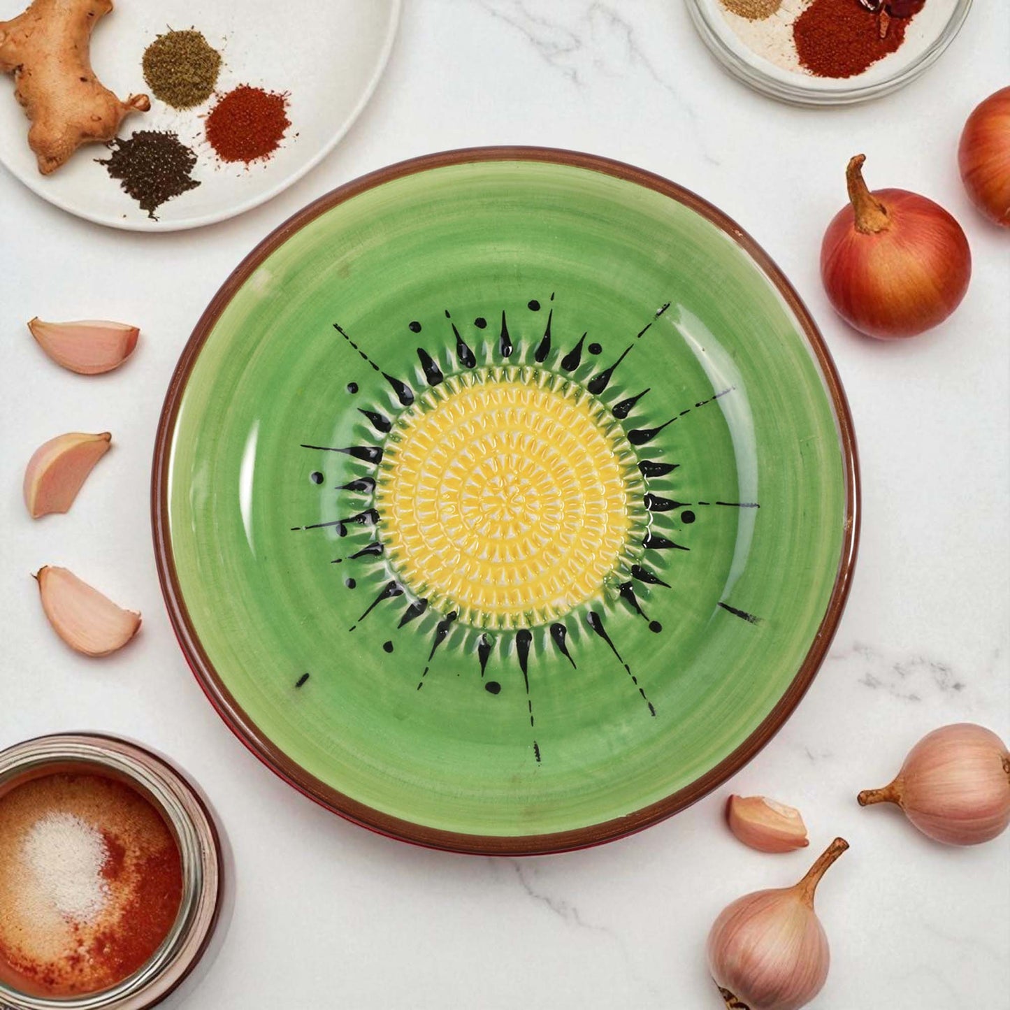 Green ceramic garlic grater bowl with yellow center and black patterns on a white surface with ingredients.