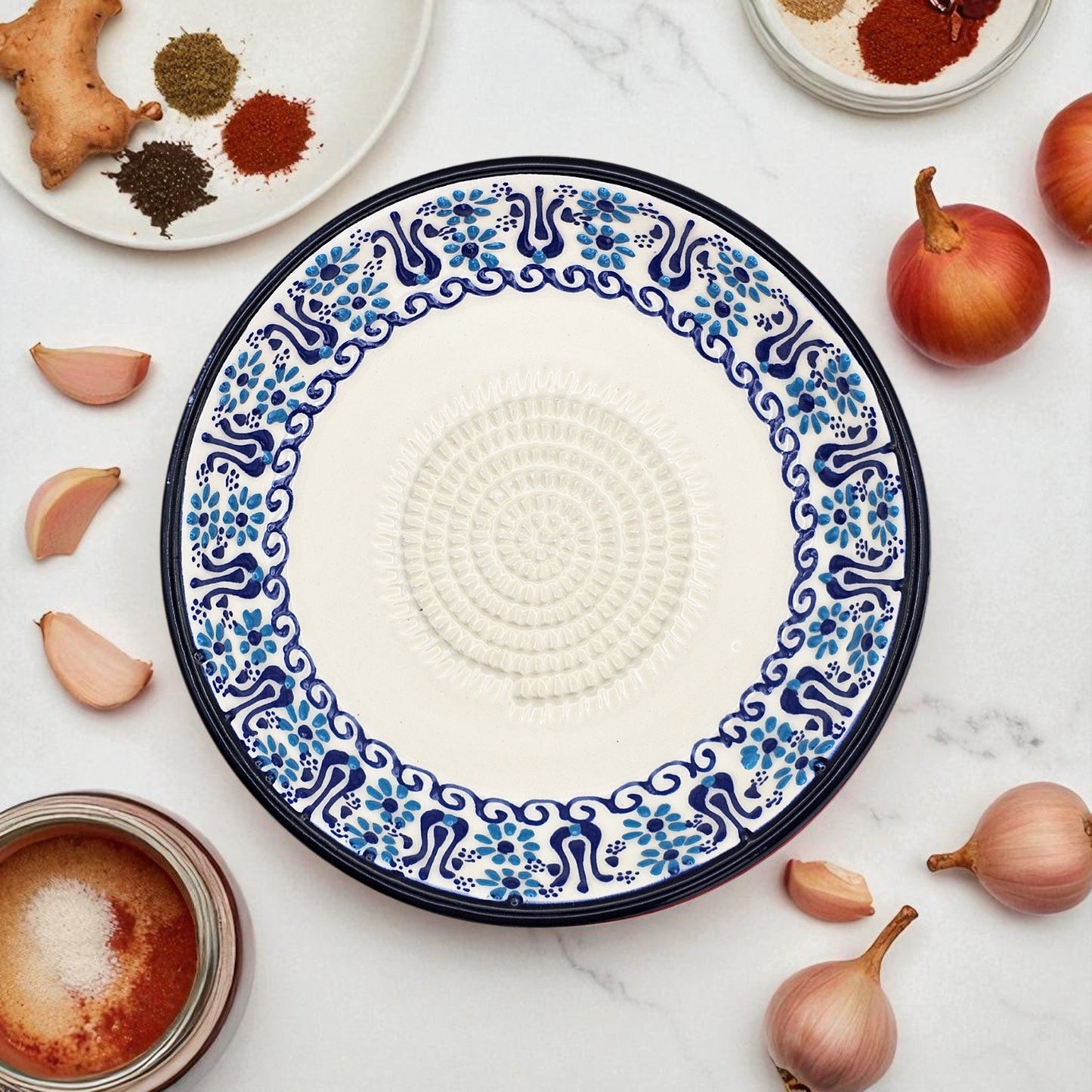 Decorative ceramic garlic grater plate with blue and white pattern on a marble surface with ingredients.