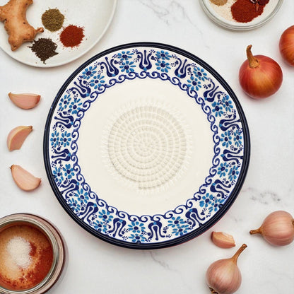 Decorative ceramic garlic grater plate with blue and white pattern on a marble surface with ingredients.