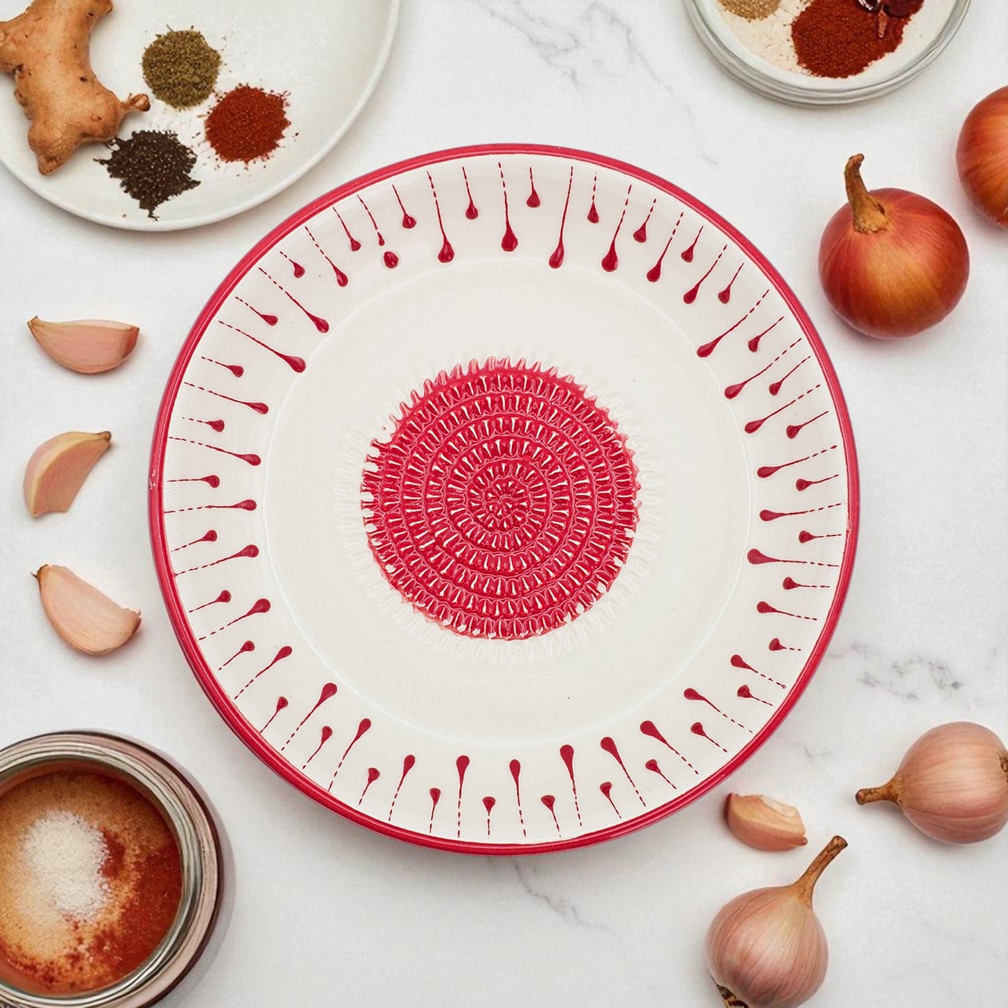 Decorative garlic grater bowl with red geometric pattern on a white surface with ingredients.
