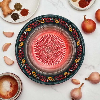 Decorative garlic grater bowl with colorful patterns on a white surface with ingredients.