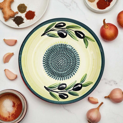 Decorative ceramic garlic grater bowl with olive design on a marble surface with ingredients.