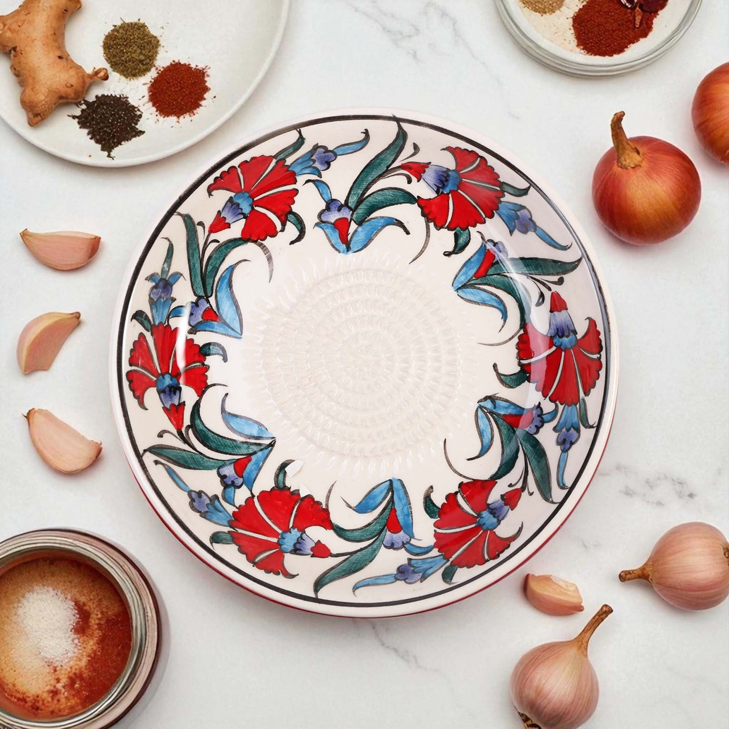 Decorative ceramic garlic grater bowl with floral patterns on a marble surface with ingredients.