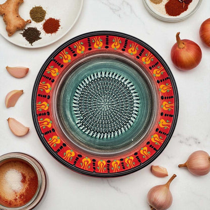 Decorative ceramic garlic grater bowl with colorful patterns on a white surface with ingredients.