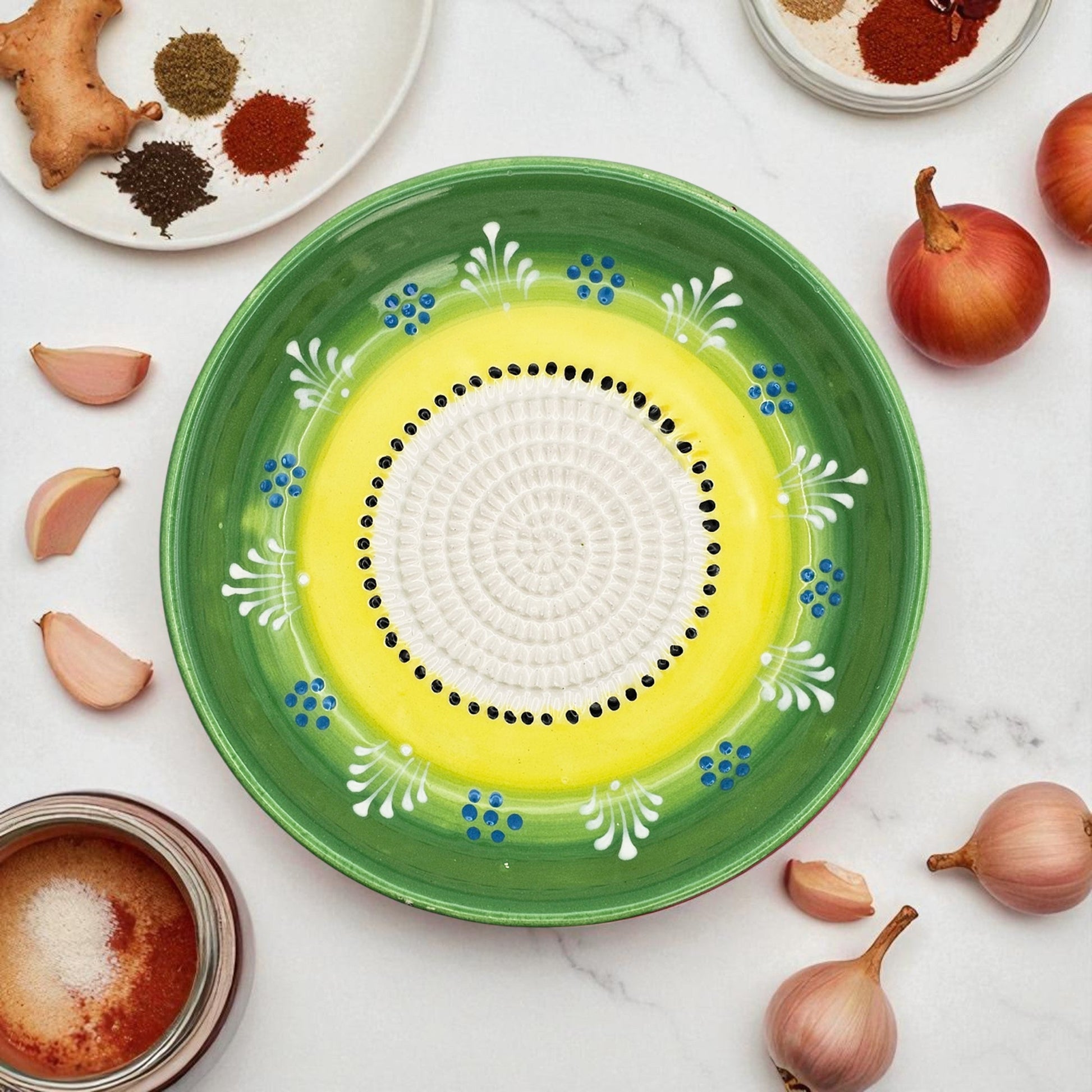 Decorative ceramic garlic grater bowl with green rim and yellow center on a marble surface with ingredients.
