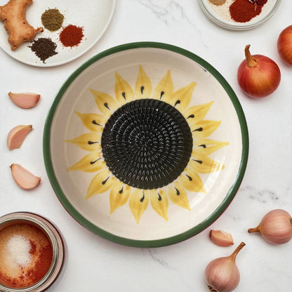 Ceramic garlic grater bowl with sunflower design on a marble surface with ingredients.