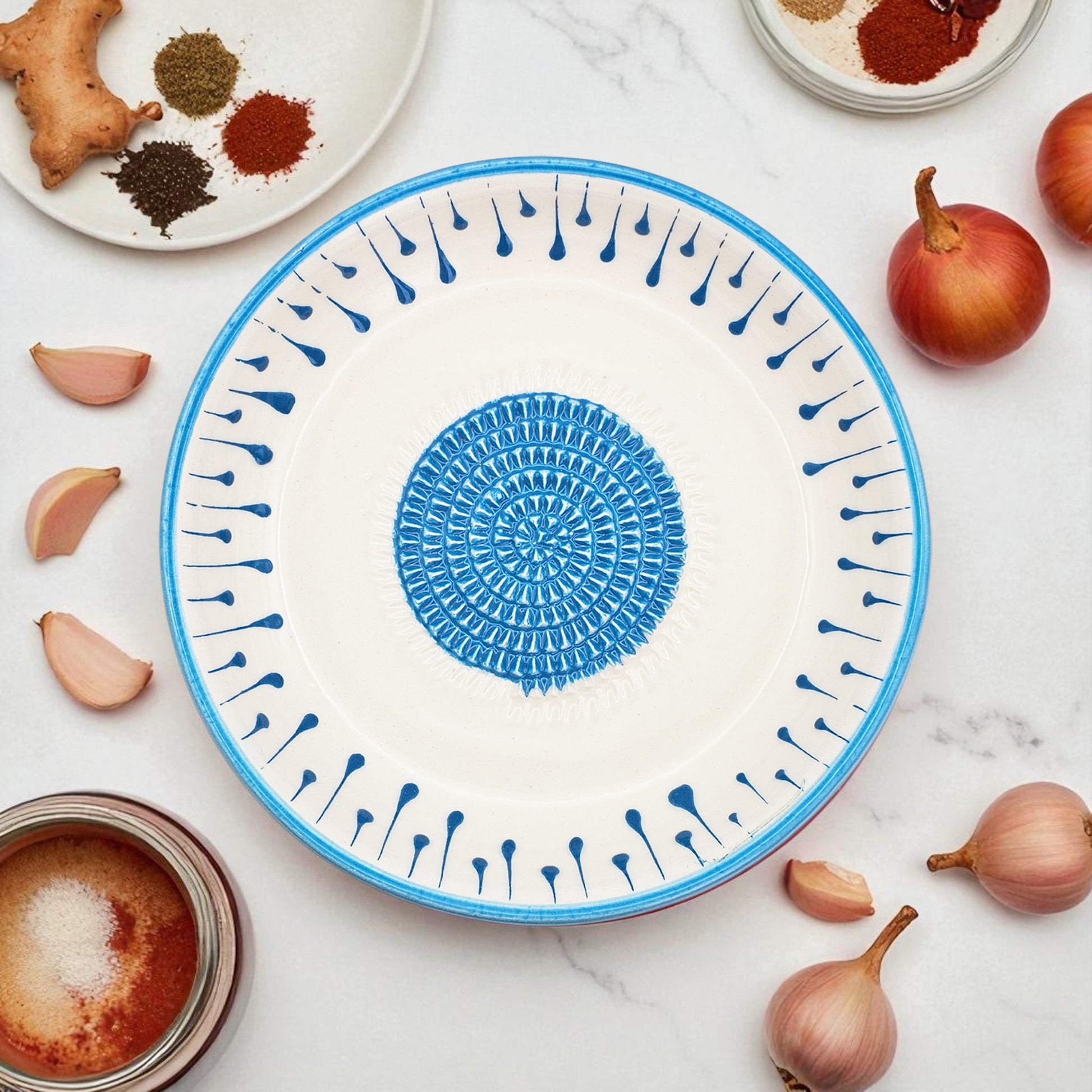 Decorative blue and white garlic grater bowl with a geometric pattern on a marble surface with ingredients.