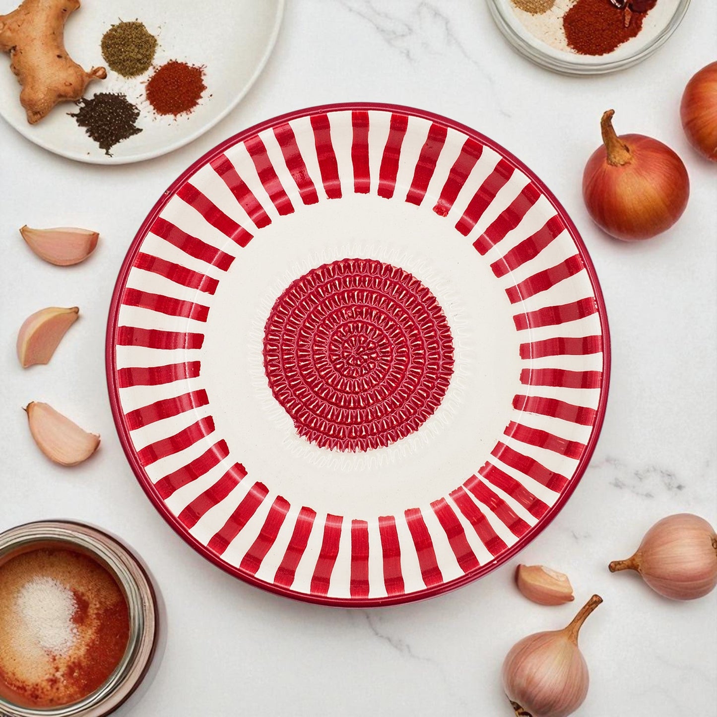 Red and white striped garlic grater bowl with decorative center on a marble surface with ingredients.