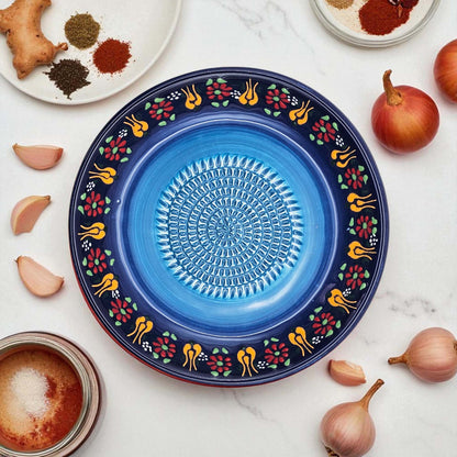 Decorative blue garlic grater bowl with floral patterns on a white surface with ingredients.