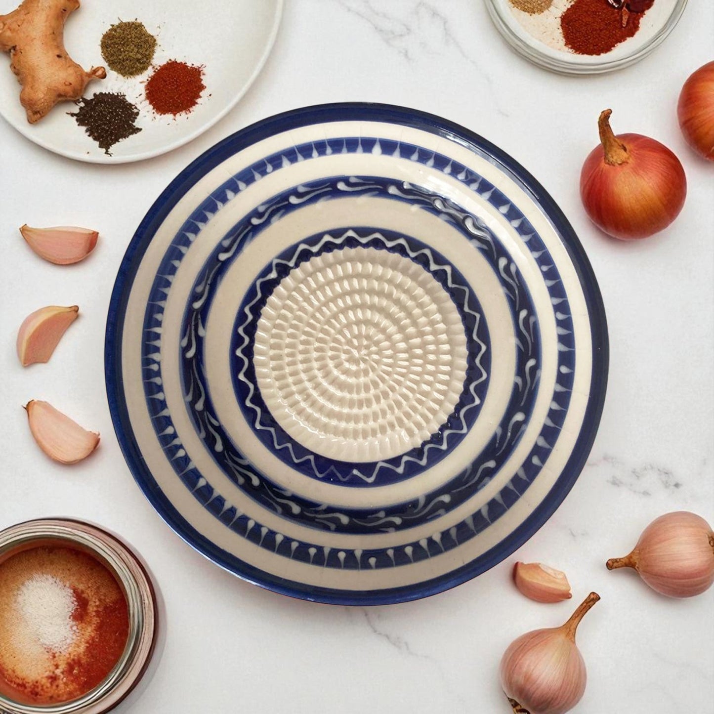Decorative blue and white ceramic garlic grater bowl on a marble surface with spices and ingredients.