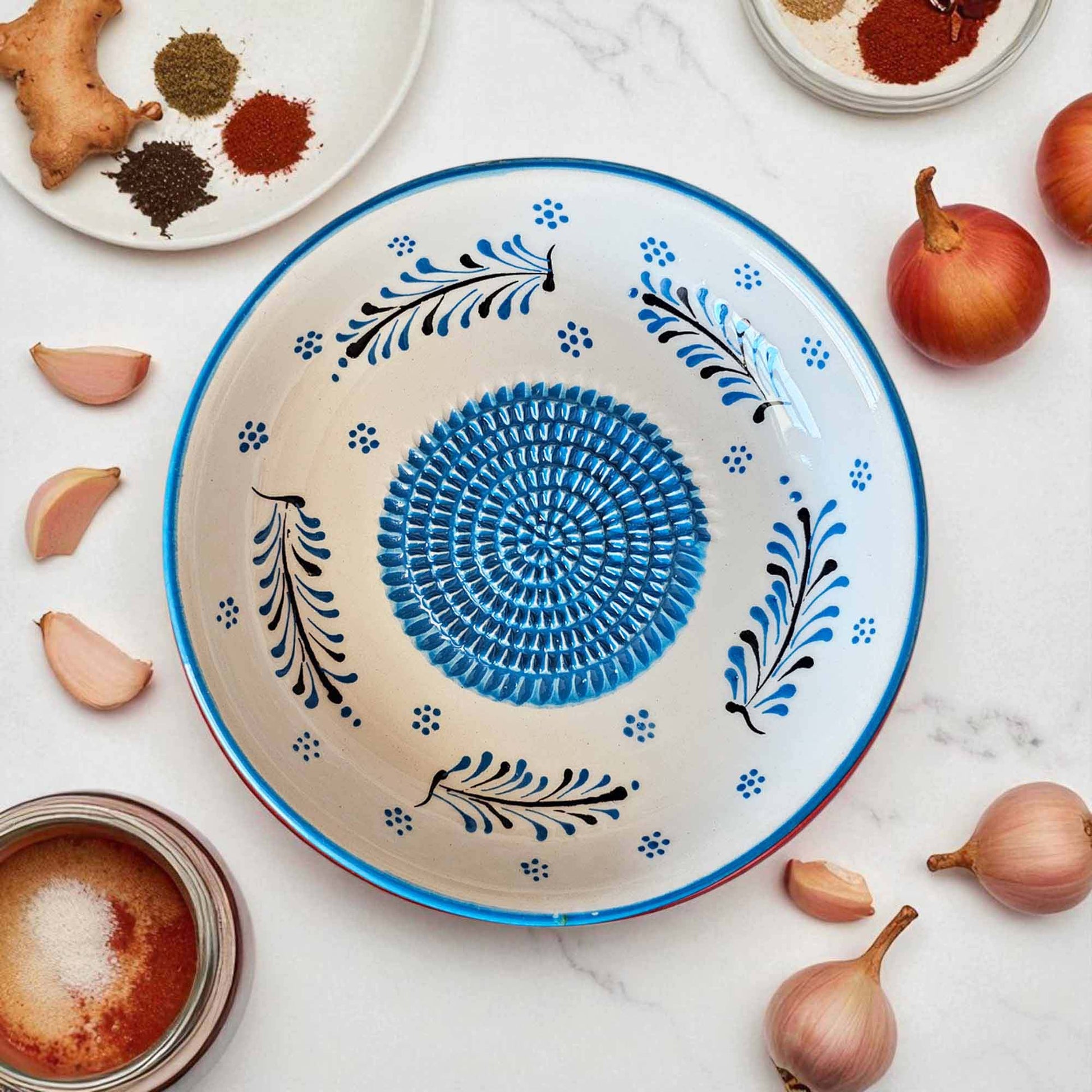 Decorative ceramic garlic grater bowl with blue and black patterns on a marble surface with ingredients.