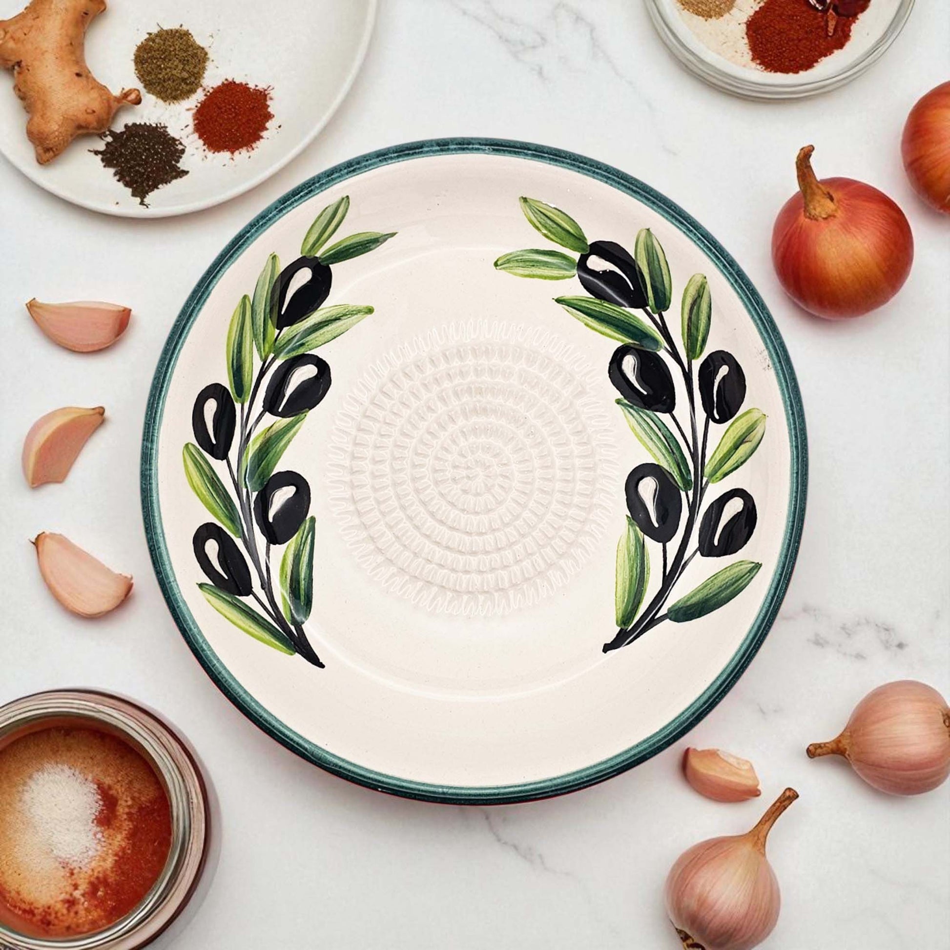 Ceramic garlic grater bowl with olive design on a marble surface with ingredients