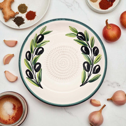 Ceramic garlic grater bowl with olive design on a marble surface with ingredients