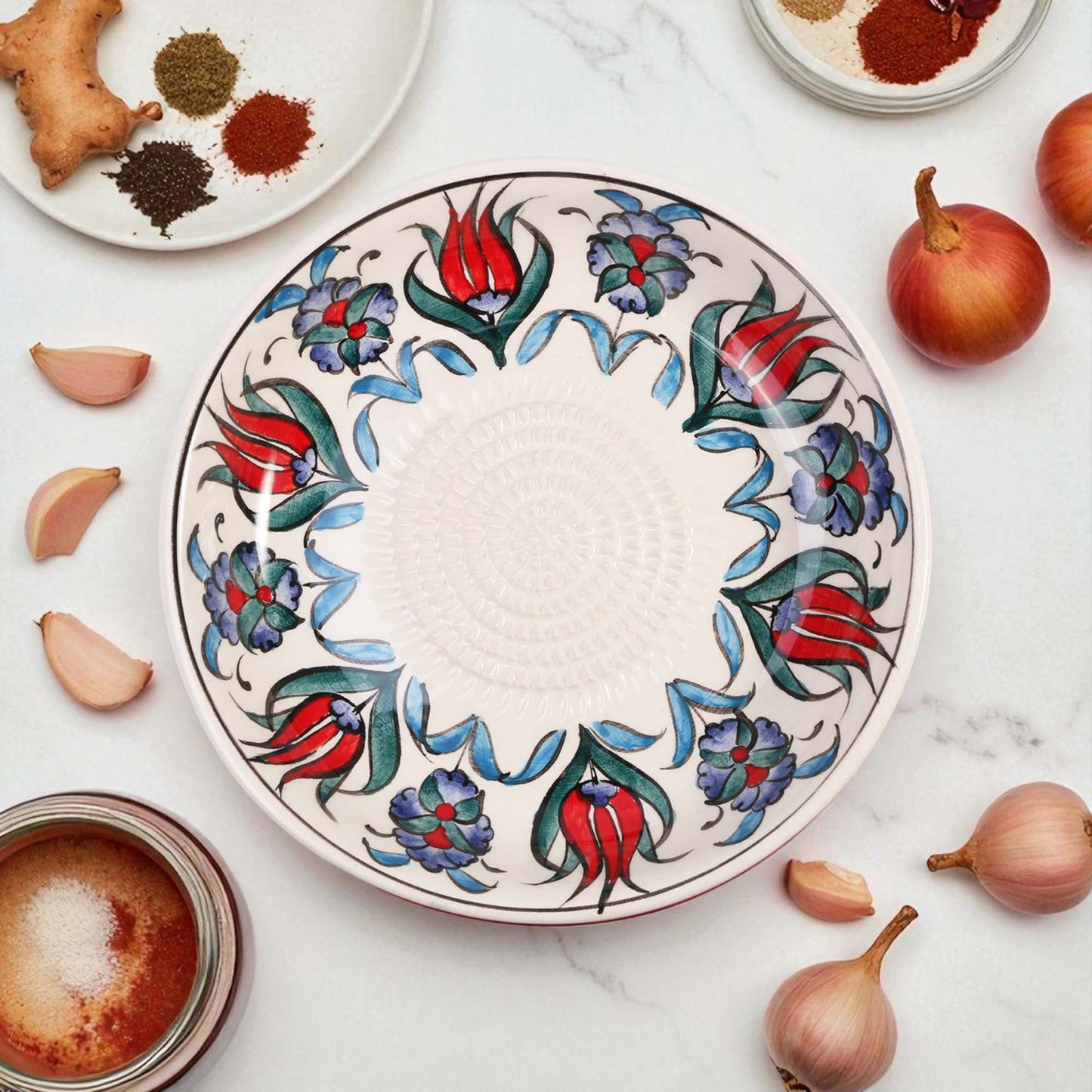 Decorative ceramic garlic grater bowl with floral patterns on a marble surface with ingredients.
