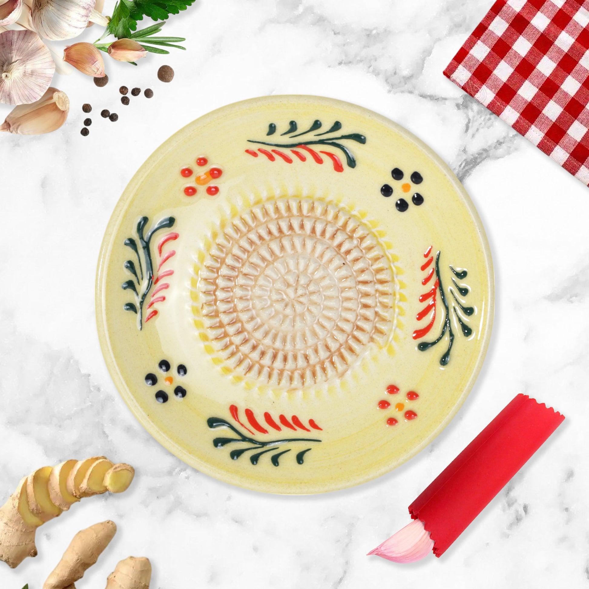 Decorative ceramic garlic grater plate with floral patterns on a marble surface with kitchen items.