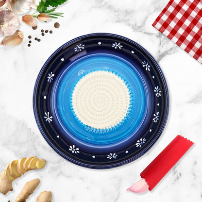 Blue ceramic garlic grater bowl with white center on a marble surface with kitchen items.