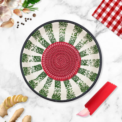 Decorative garlic grater bowl with a red center and green and white pattern on a marble surface with kitchen items.