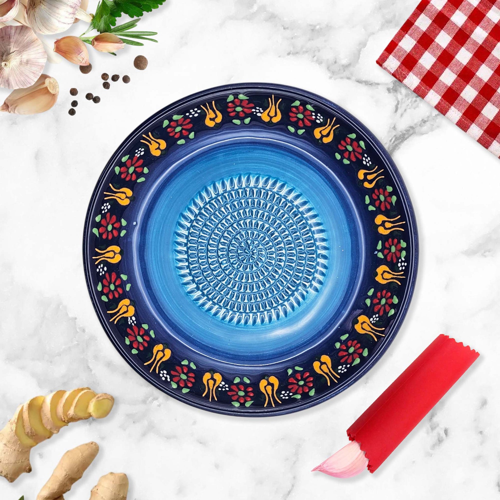 Decorative blue garlic grater bowl with floral patterns on a marble surface with ginger and a red checkered cloth.