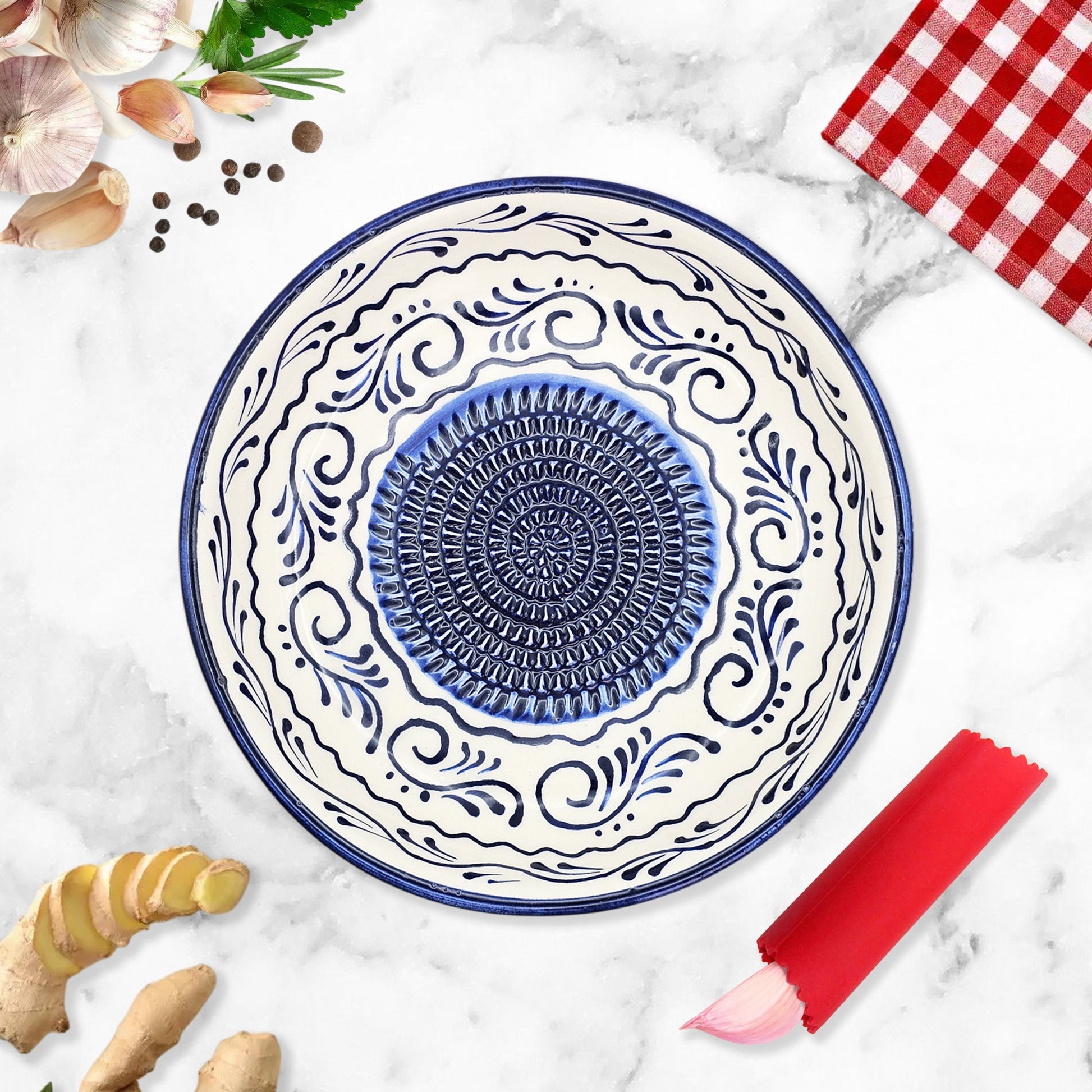 Decorative ceramic garlic grater bowl with blue and white patterns on a marble surface with ginger and a red checkered cloth.