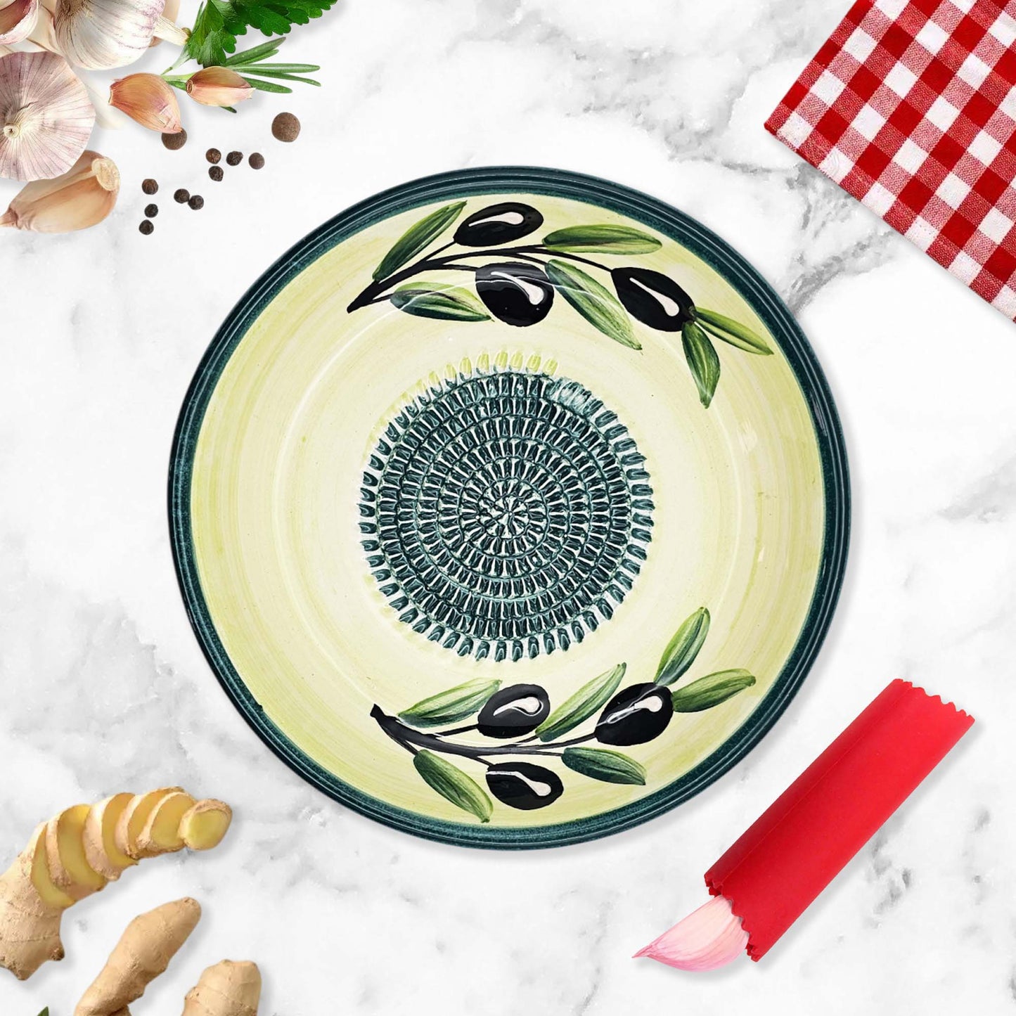 Decorative ceramic garlic grater bowl with olive design on a marble surface with kitchen items.