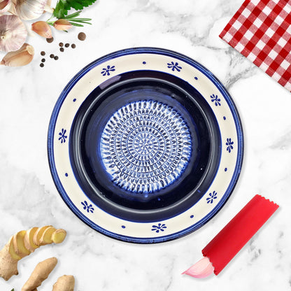 Decorative blue ceramic garlic grater bowl with floral patterns on a marble surface with kitchen items.