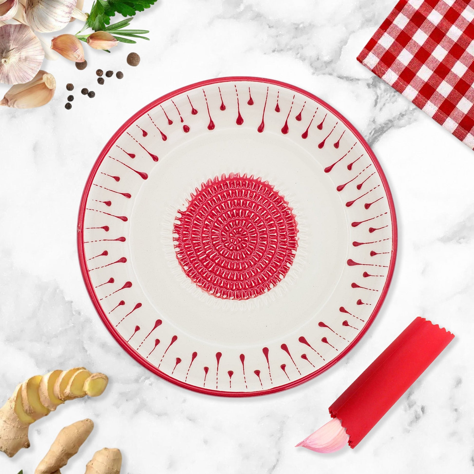 Round silicone mat with red border and textured garlic grater bowl on a marble surface with kitchen items.