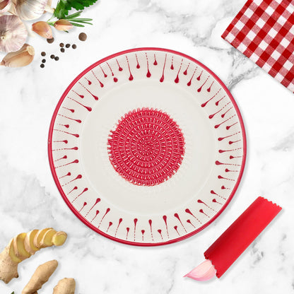 Round silicone mat with red border and textured garlic grater bowl on a marble surface with kitchen items.