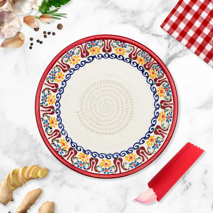 Decorative garlic grater bowl with colorful floral pattern on a marble surface with ginger and a checkered cloth.