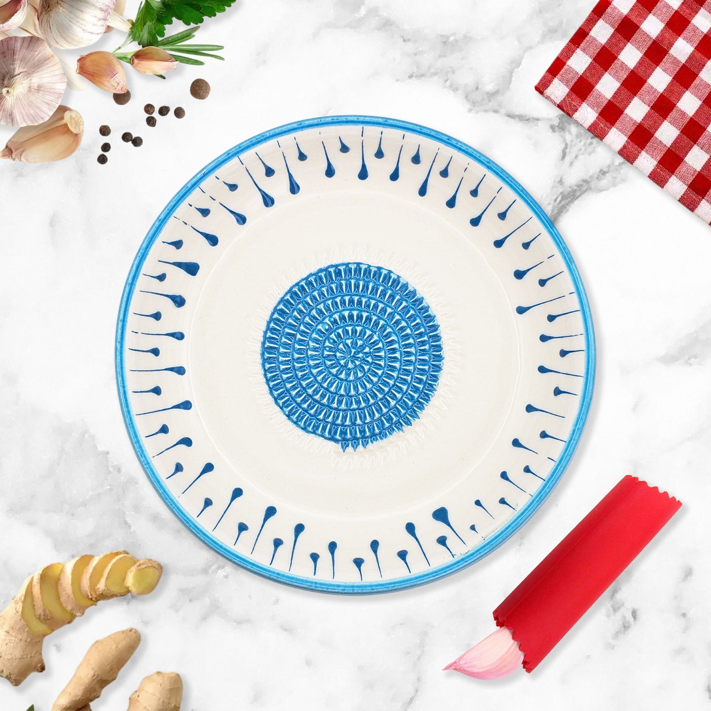 Ceramic garlic grater bowl with blue decorative pattern on a marble surface with ginger and a red checkered cloth.