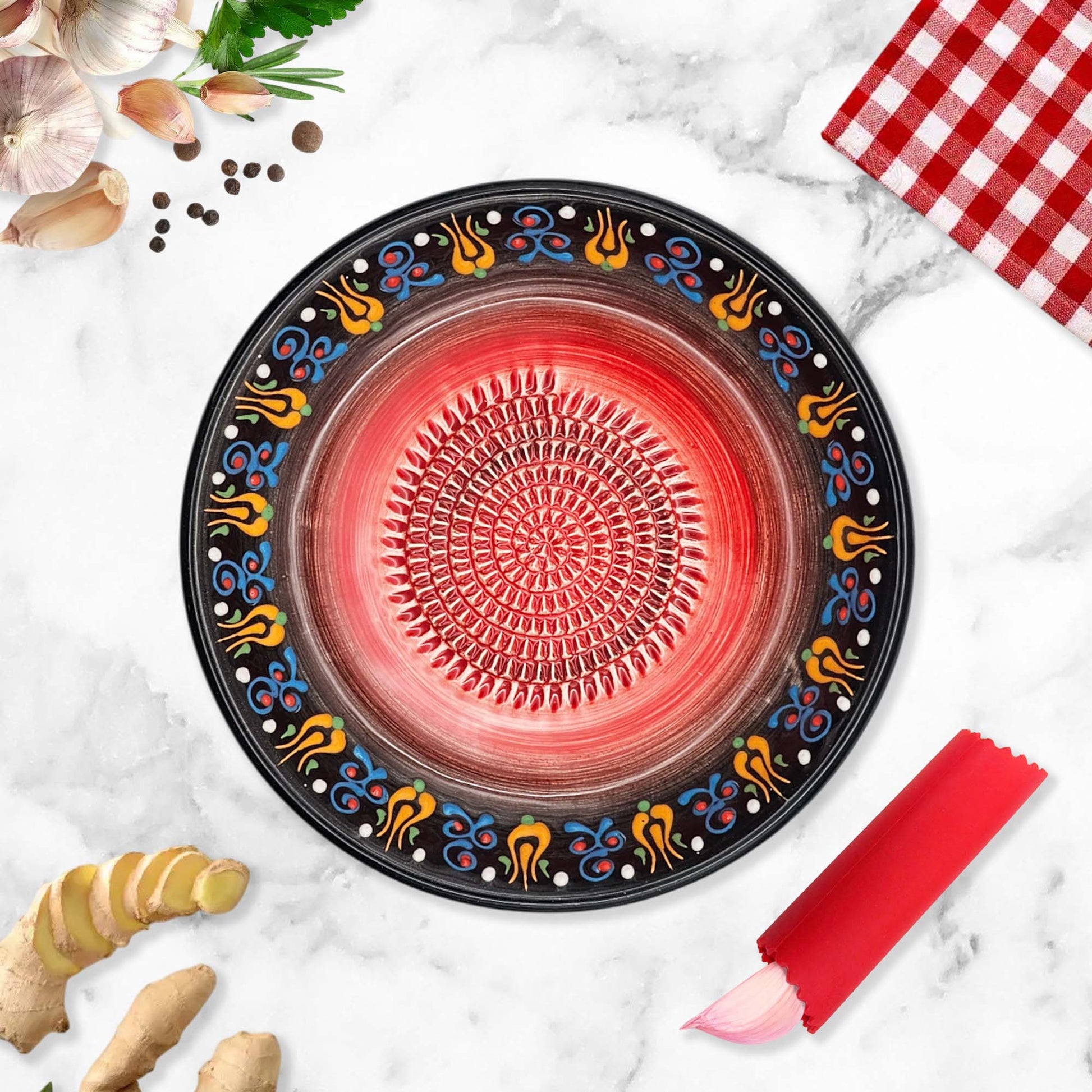 Decorative garlic grater bowl with colorful patterns on a marble surface with ginger and a red checkered cloth.