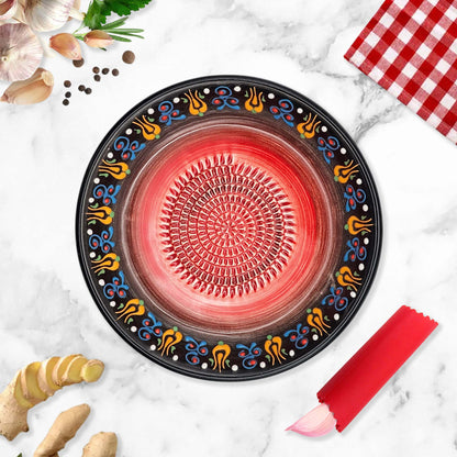 Decorative garlic grater bowl with colorful patterns on a marble surface with ginger and a red checkered cloth.