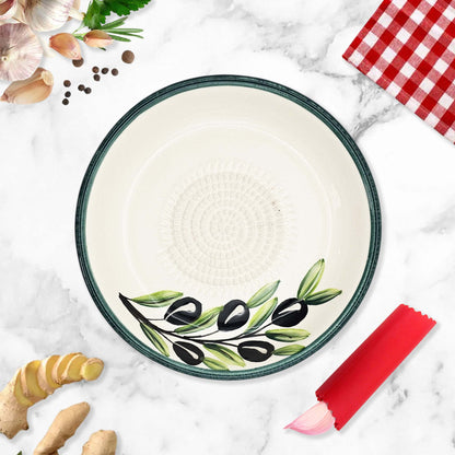 Ceramic garlic grater bowl with olive design on a marble surface with kitchen items.