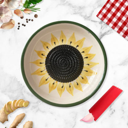 Ceramic garlic grater bowl with sunflower design on a marble surface with ginger and a red checkered cloth.