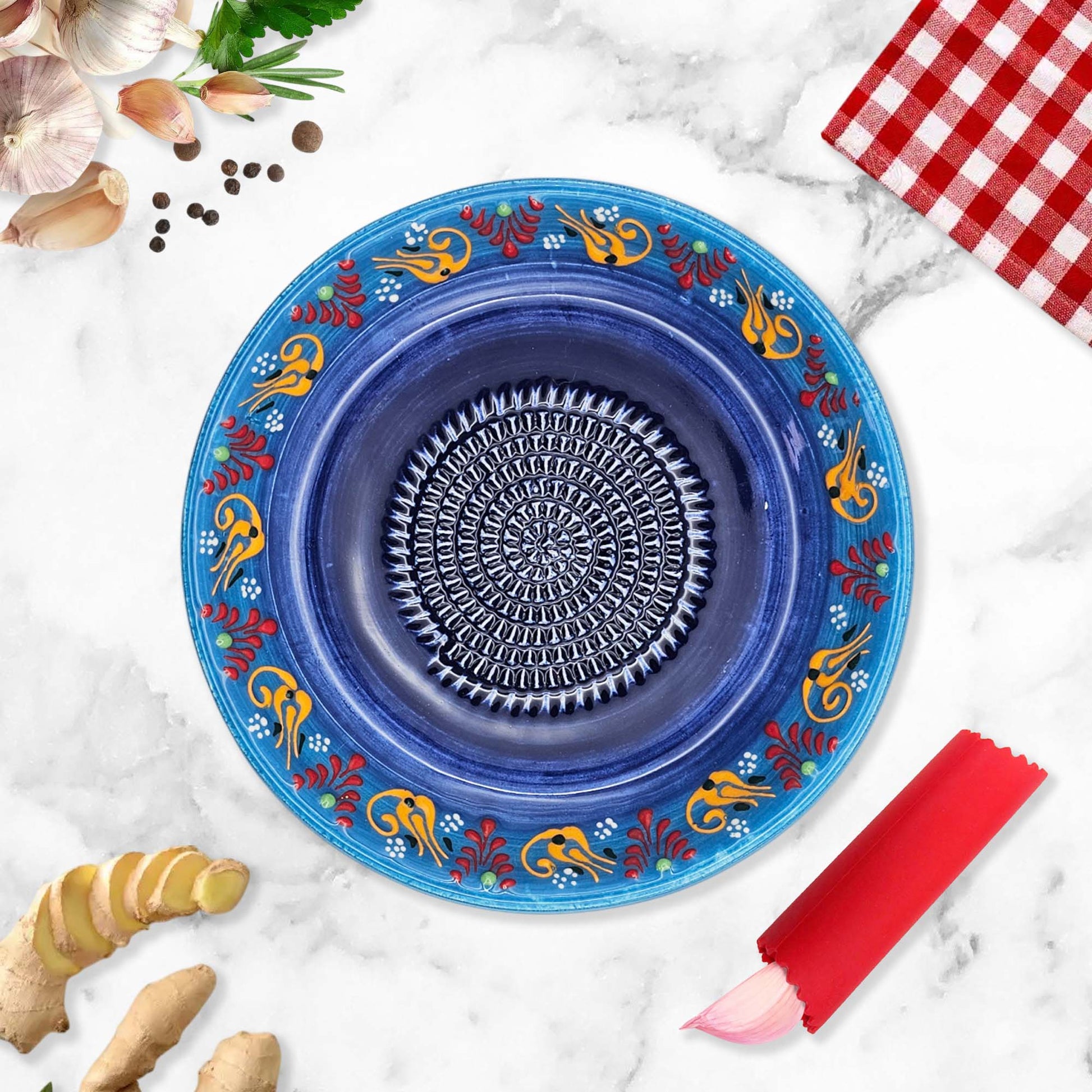 Decorative blue garlic grater bowl with floral patterns on a marble surface with ginger and a red checkered cloth.