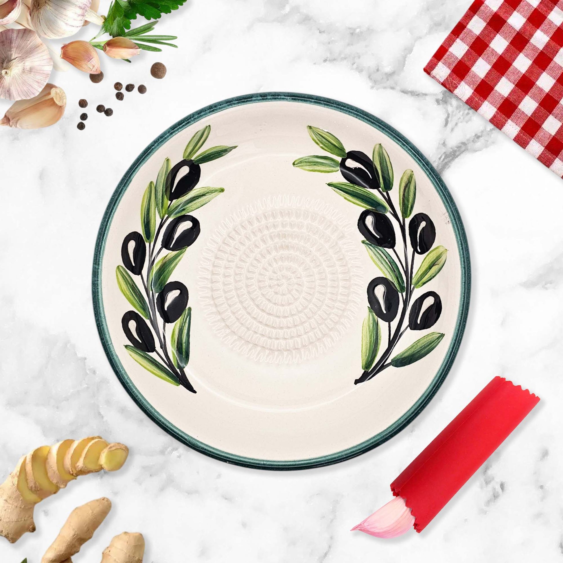 Ceramic garlic grater bowl with olive design on a marble surface with ingredients.
