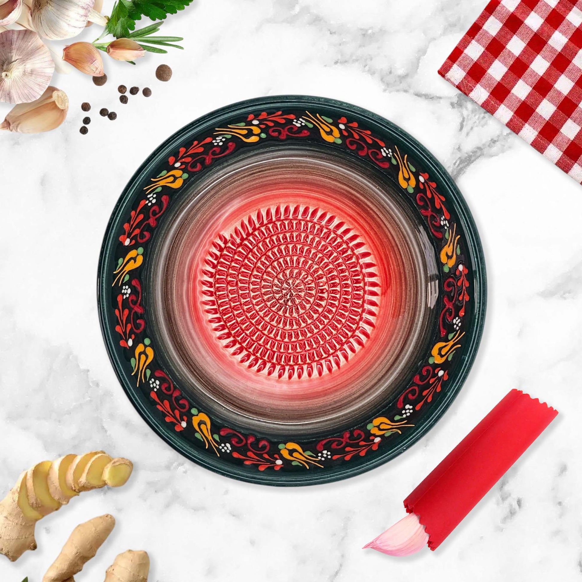 Decorative ceramic garlic grater bowl with floral patterns on a marble surface with ginger and a red checkered cloth.