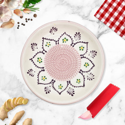 Decorative ceramic garlic grater bowl with intricate patterns on a marble surface with ginger and a red checkered cloth.