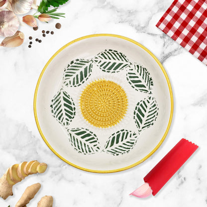 Decorative garlic grater bowl with leaf pattern on a marble surface with kitchen items.