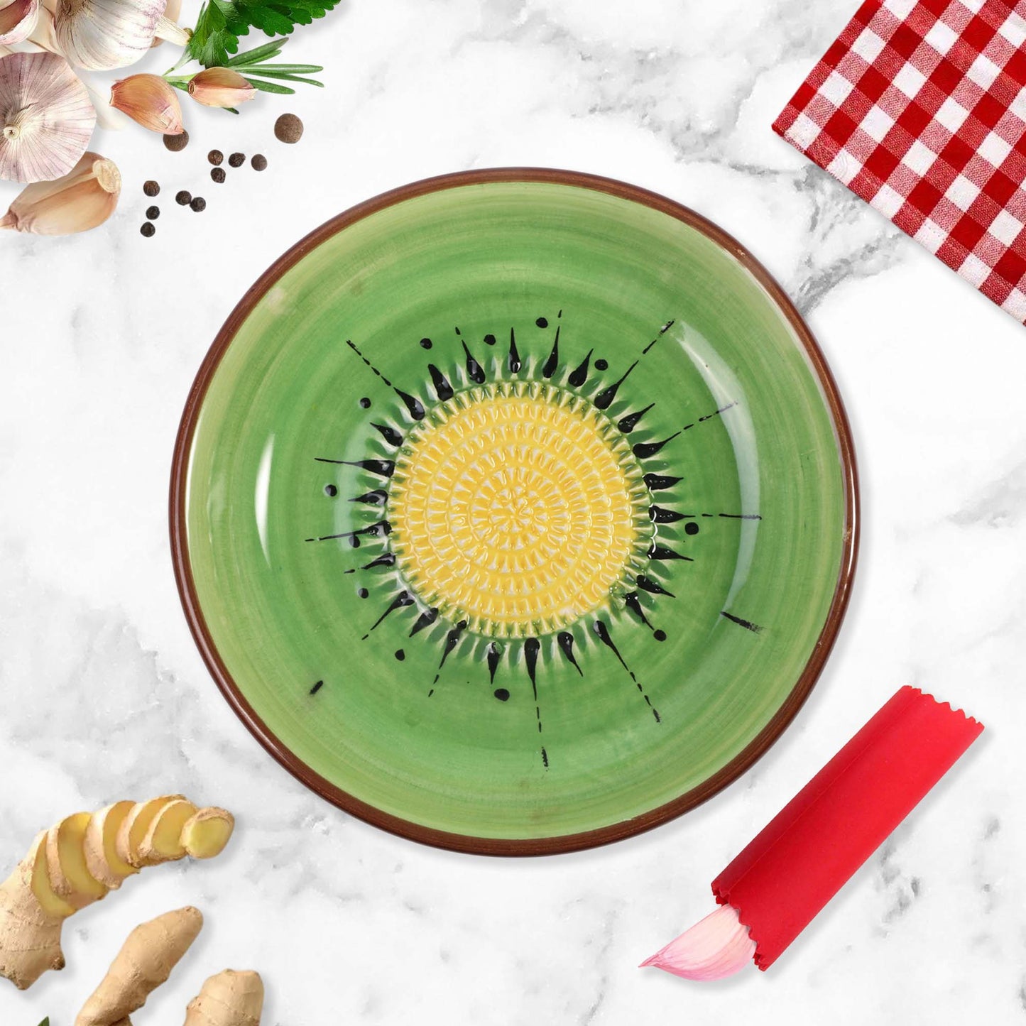 Green ceramic garlic grater bowl with yellow center and black patterns on a marble surface with kitchen items.