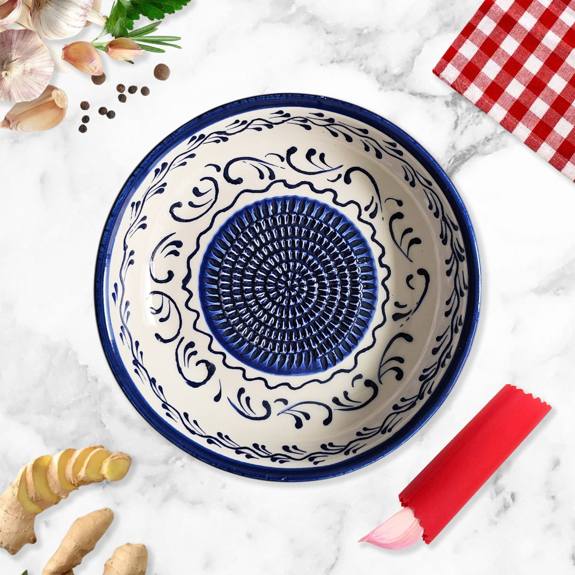 Decorative ceramic garlic grater bowl with blue and white pattern on a marble surface with ginger and a red checkered cloth.