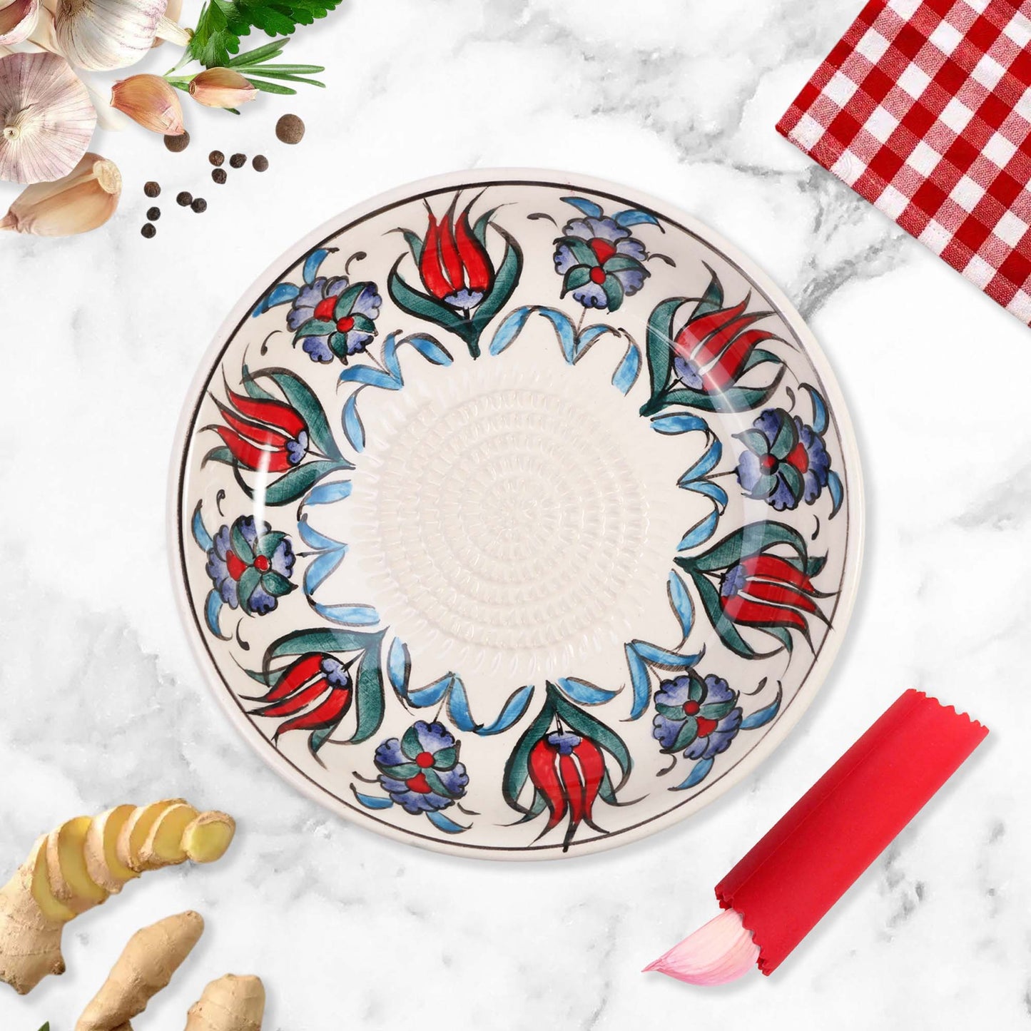 Decorative ceramic garlic grater bowl with floral patterns on a marble surface with kitchen items.