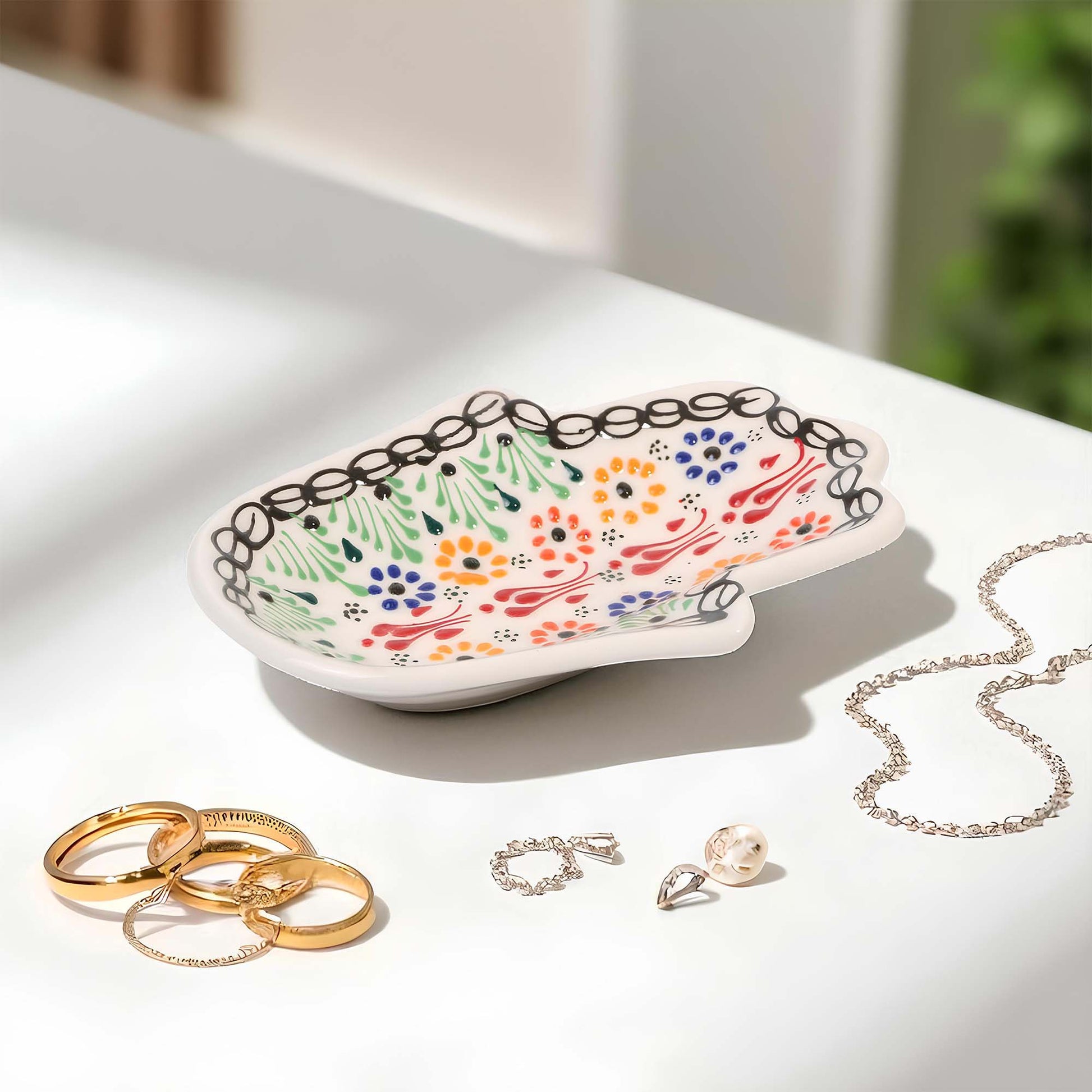 Decorative jewelry dish with floral patterns on a white surface with jewelry items.