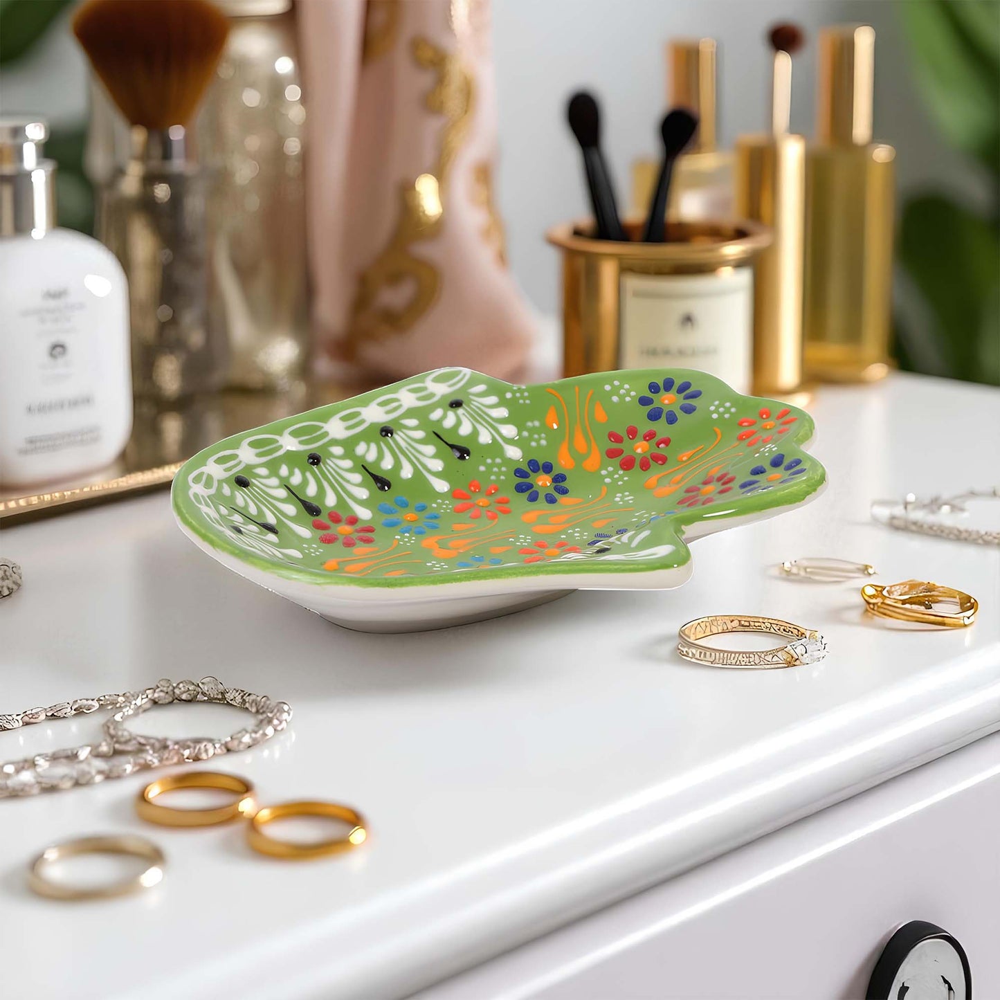 Decorative green lizard-shaped tray with colorful patterns on a white surface with jewelry.